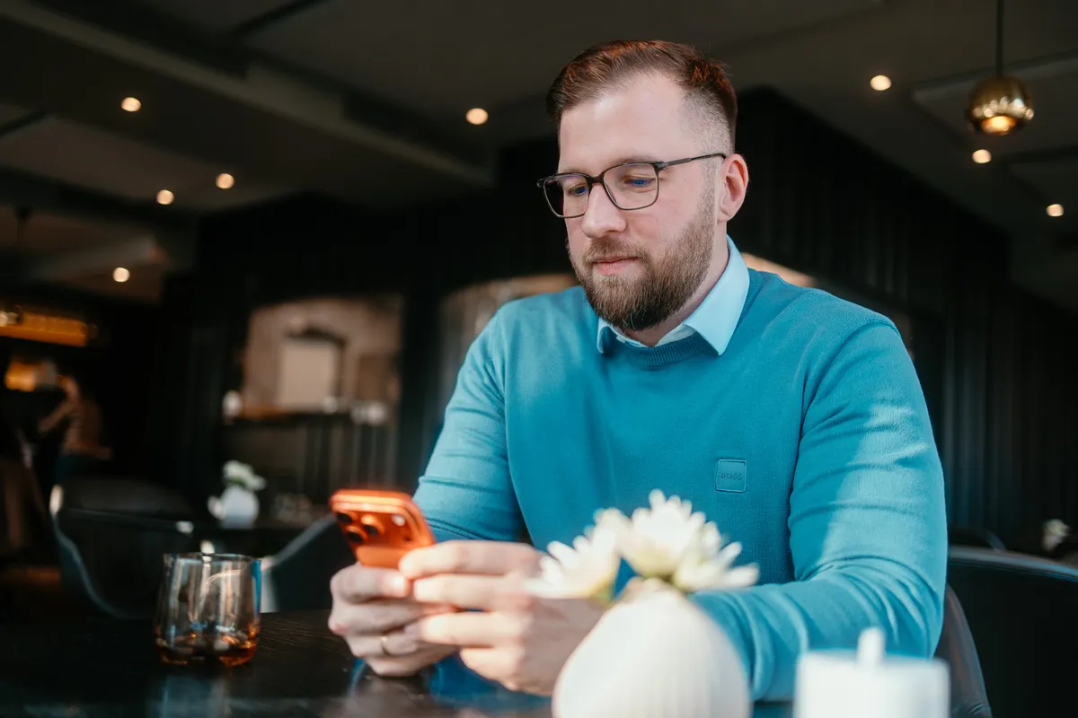 Marvin Jennrich sitzt in einem Restaurant am Tisch und tippt auf seinem Smartphone