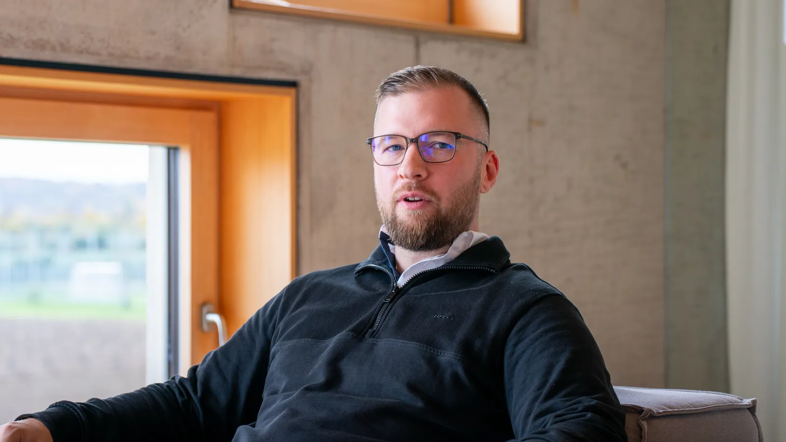 Marvin Jennrich sitzt in einem Sichtbeton-Raum am Fenster und ist im Gespräch