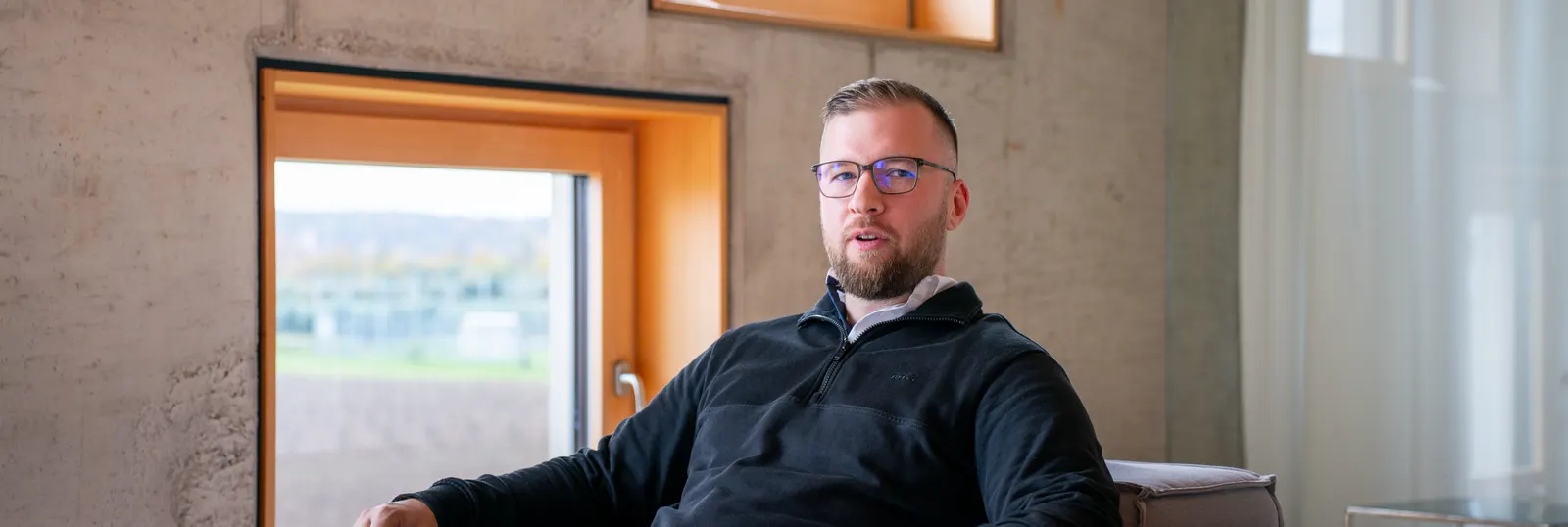 Marvin Jennrich, sitzend vor einer Sichtbetonwand