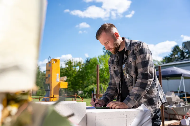 Marvin Jennrich beugt sich auf der Baustelle über einen Plan auf der Mauer und macht Notizen