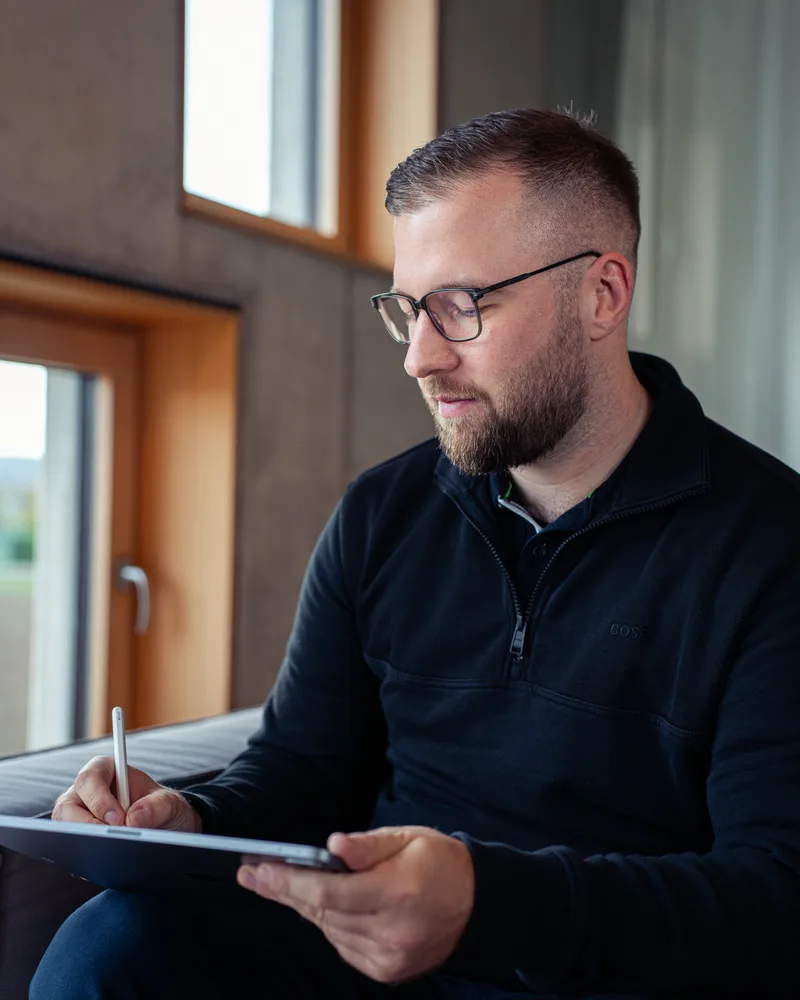 Marvin Jennrich arbeitet mit Stift am Tablet, im Hintergrund Sichtbeton und Fenster
